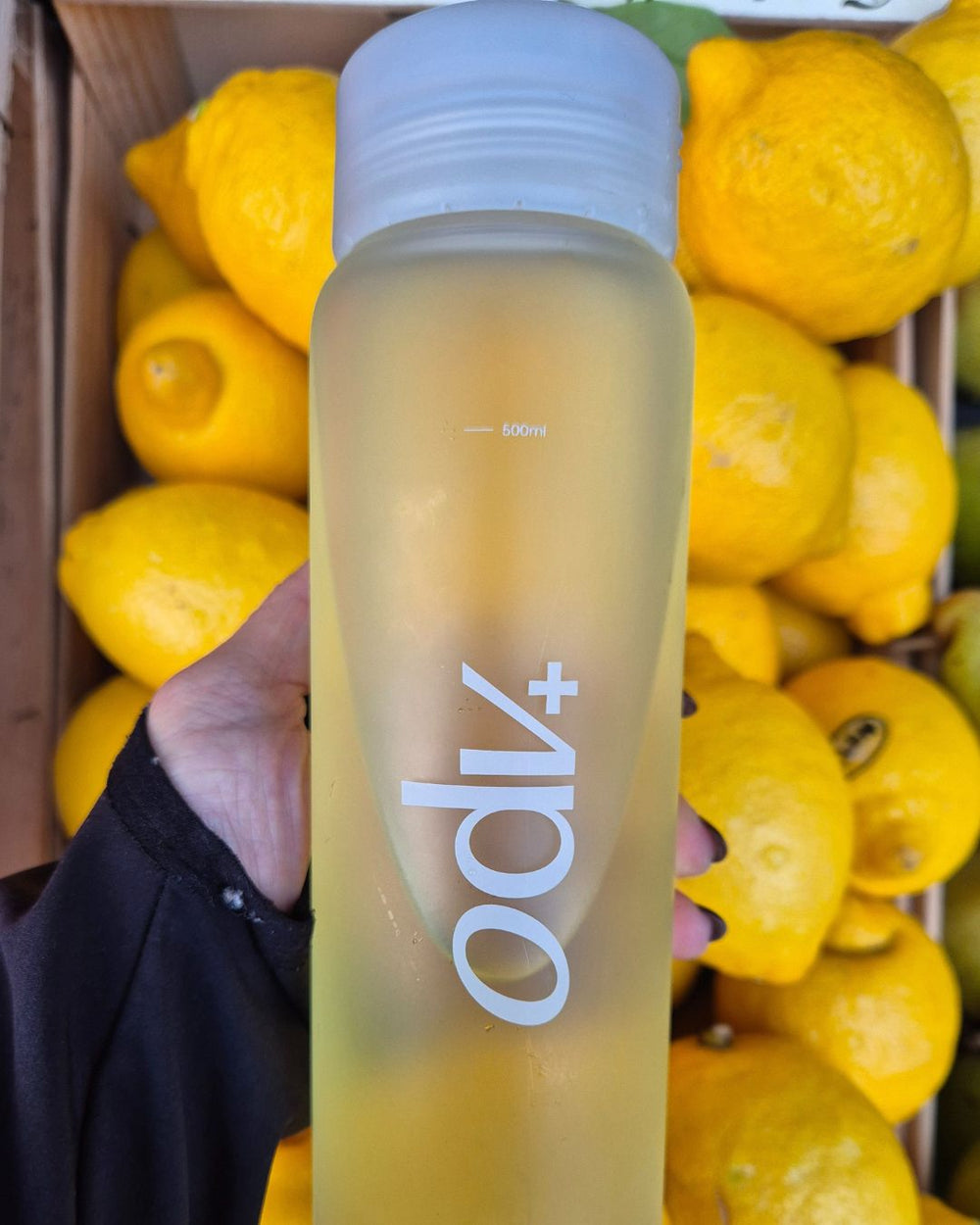 Clear bottle with white lid and 'adpo' branding held in front of lemons